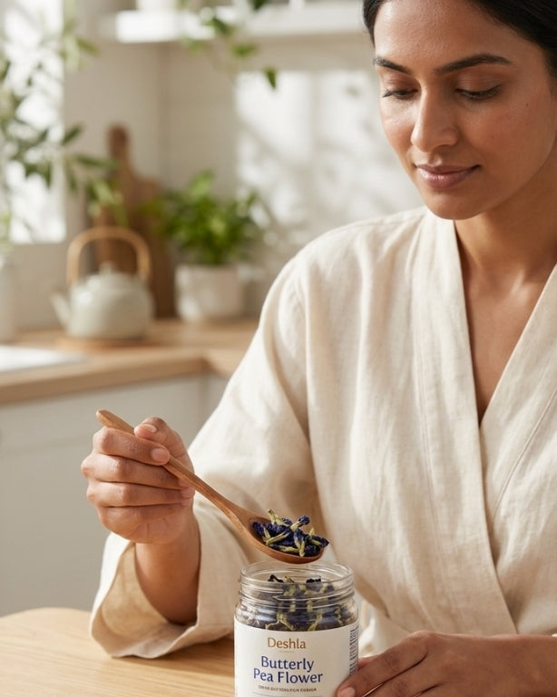 Woman in a kitchen holding a jar of 'Butterfly Pea Flower' and a wooden spoon.