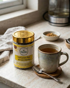 Deshla Fenugreek Plus Herbal Infusion canister next to a cup of tea on a kitchen counter.