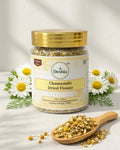 Jar of Deshla Chamomile Dried Flower with a wooden spoon and chamomile flowers on a light background