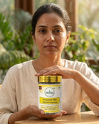 Woman holding a jar of Deshla Tonmugreek Plus Herbal Infusion with greenery in the background