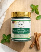 Deshla Spirulina powder jar with mint leaves and cinnamon sticks on a wooden surface