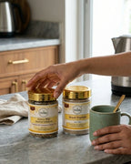 Person holding a jar of herbal infusion on a kitchen counter with another jar and a mug.