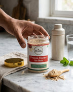 Desha Protein Powder for Men jar on a marble surface with a hand reaching towards it.