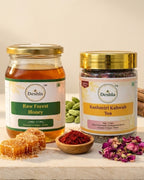 Two jars of Deshla honey and tea on a wooden surface with honeycomb and tea leaves.