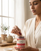 Woman holding a jar of Deshla Natural Red Hibiscus Dried Flower with a teacup and teapot in the background.