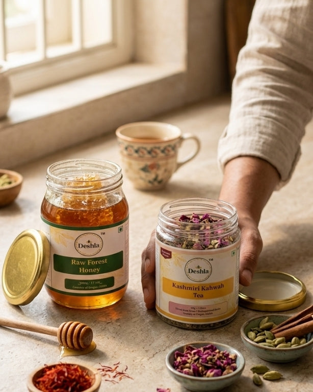Two jars of Deshla honey and Kashmiri Kahwa tea on a table with a cup and spices.