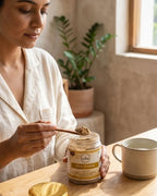 Woman in a white robe scooping a spoonful of a product from a jar labeled 'Doshisha' on a wooden table.